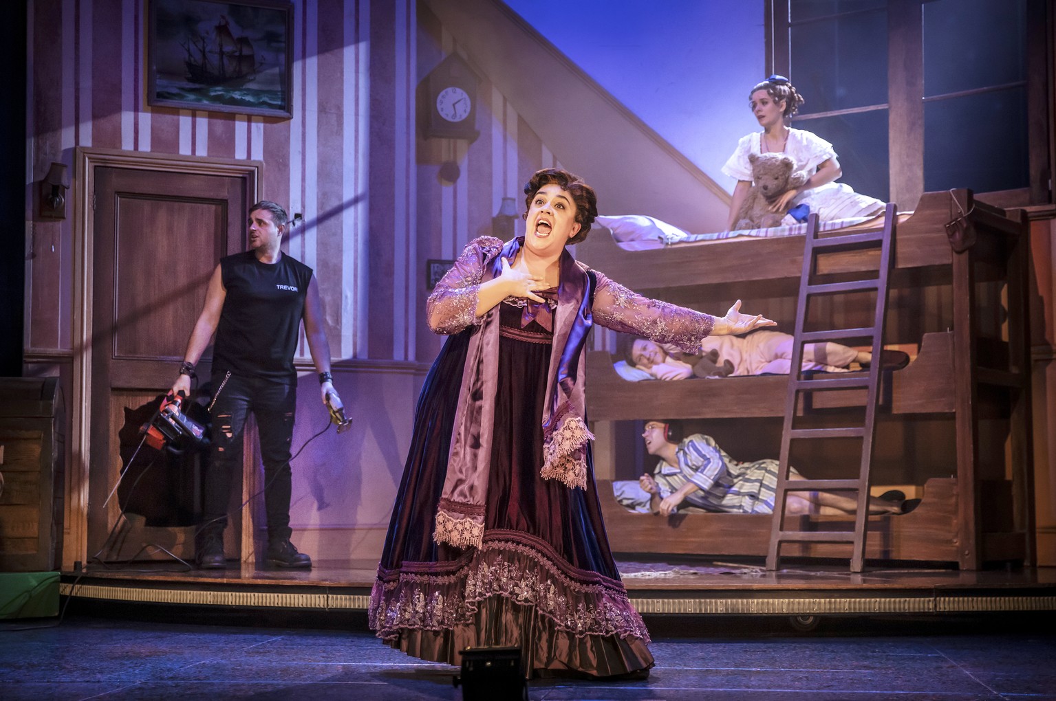 A lively theatre scene with actors in costume performing a comedic scene from Peter Pan Goes Wrong.