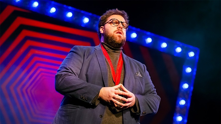 A performer in a dramatic pose, surrounded by vibrant lighting and abstract set design.