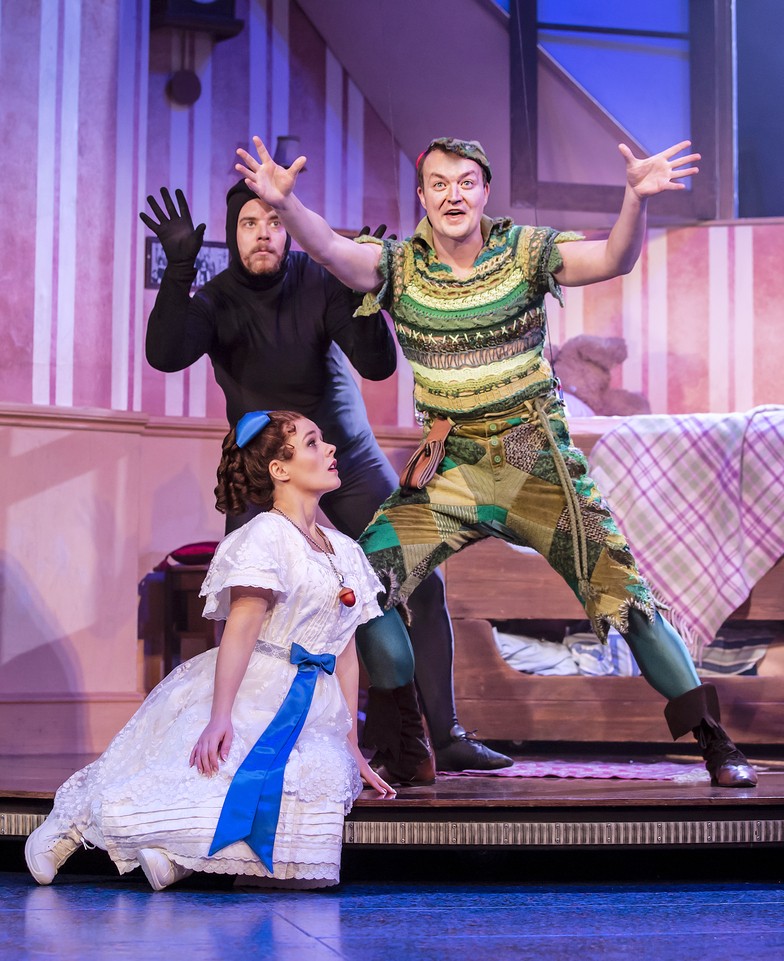 A theatrical scene from "Peter Pan Goes Wrong" featuring actors in vibrant costumes on stage.