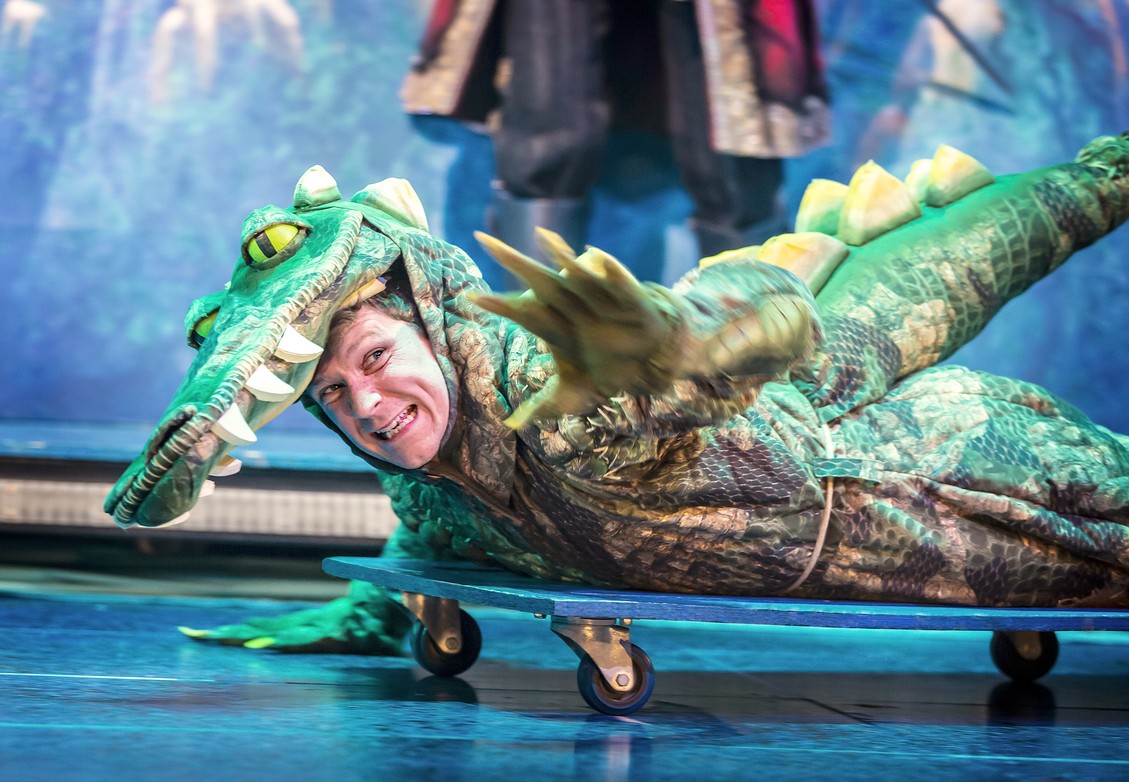 A theatrical scene from "Peter Pan Goes Wrong" featuring actors in vibrant costumes on stage.