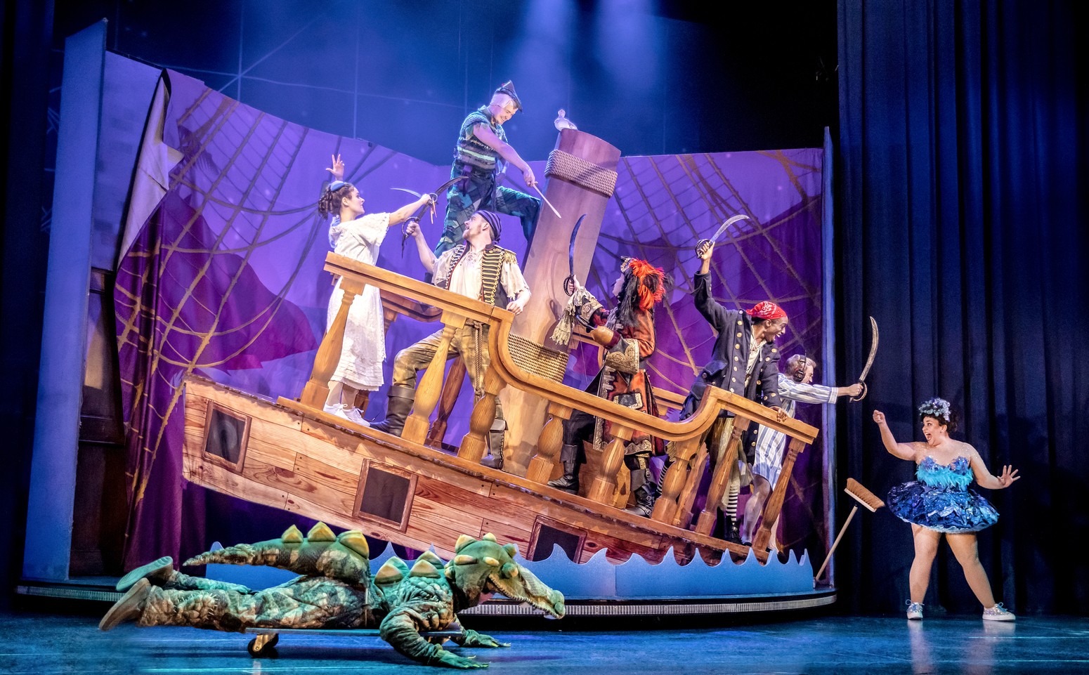 A theatrical scene featuring actors in costumes, performing on stage with dramatic lighting.