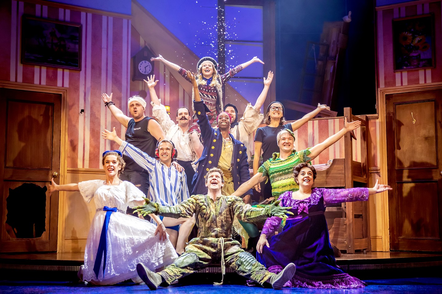 A theatrical scene from "Peter Pan Goes Wrong" featuring actors in vibrant costumes on stage.