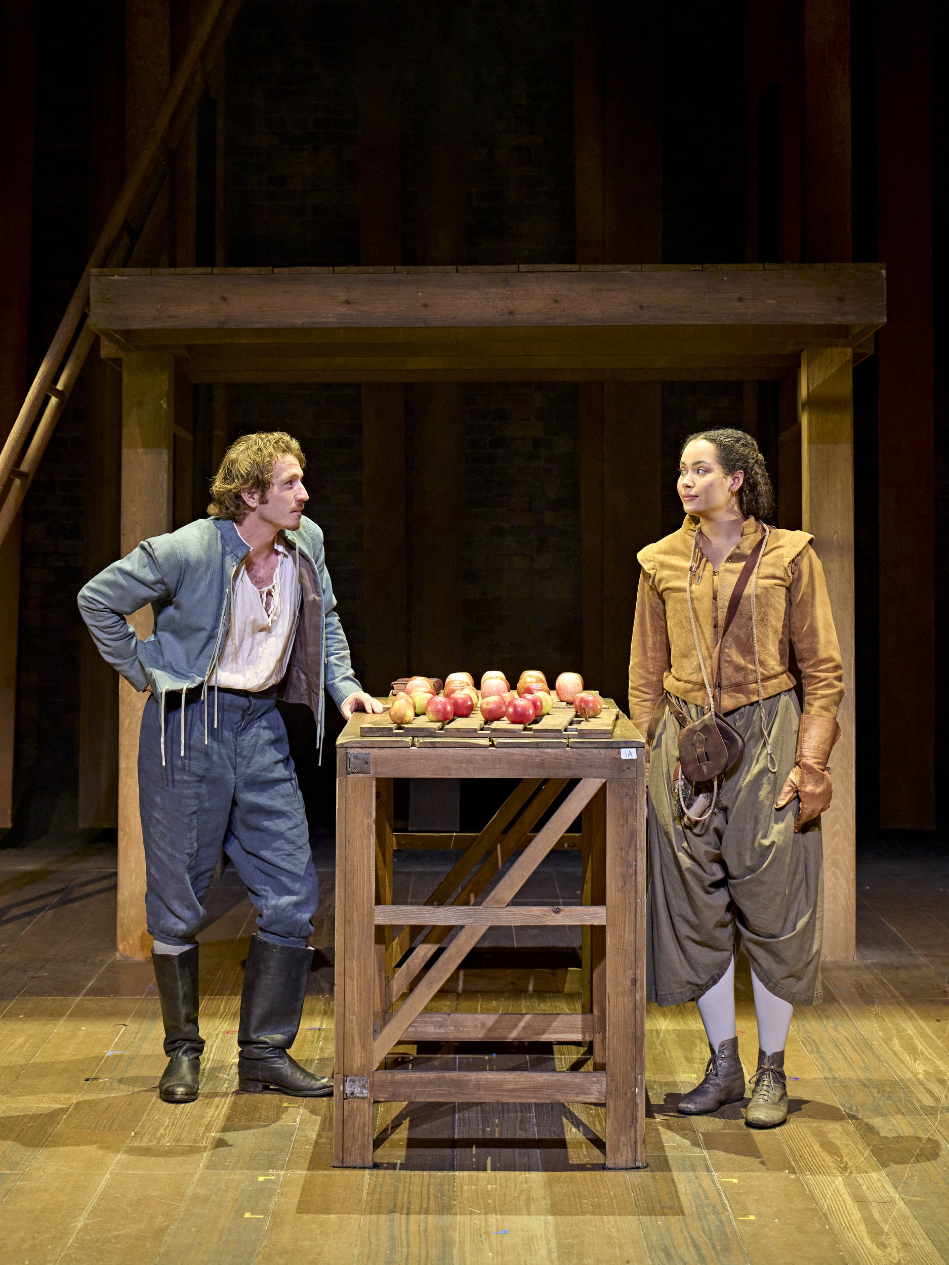 A diverse group of actors in period costumes, posed together on stage during a performance.