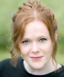 Alana Ramsey smiling, wearing a blue blouse, with long brown hair and a neutral background.
