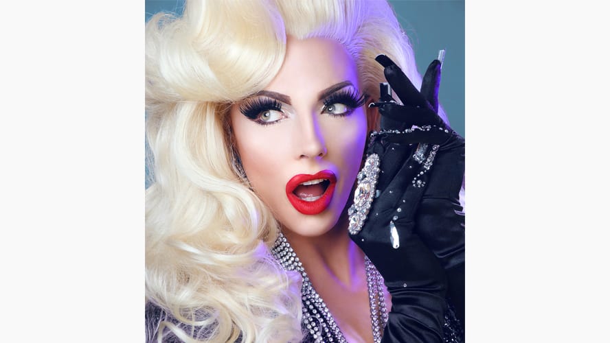 Alyssa Edwards poses with a bright smile, wearing a vibrant, sequined outfit and dramatic makeup.