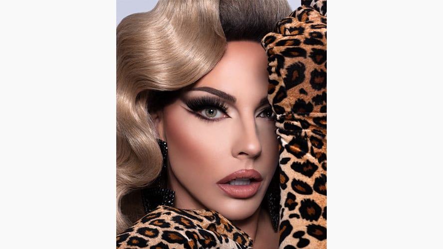 Alyssa Edwards poses confidently, wearing a vibrant sequined outfit and styled hair, smiling at the camera.