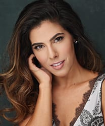 Aimie Atkinson smiling, wearing a stylish black dress with shoulder-length hair and natural makeup.