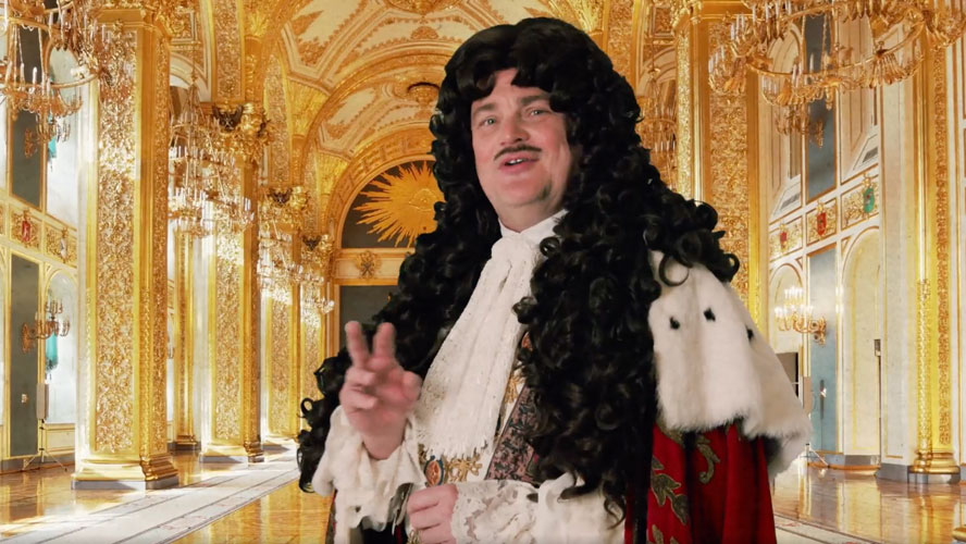 Al Murray wearing a historical costume, standing in front of the Crown Jewels display.
