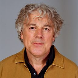 Alan Davies with short dark hair, smiling against a neutral background.