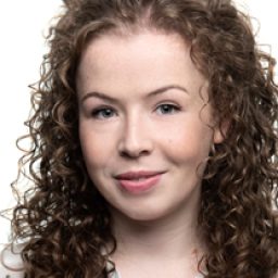 Amy Trigg smiling, with shoulder-length brown hair and wearing a black top against a neutral background.