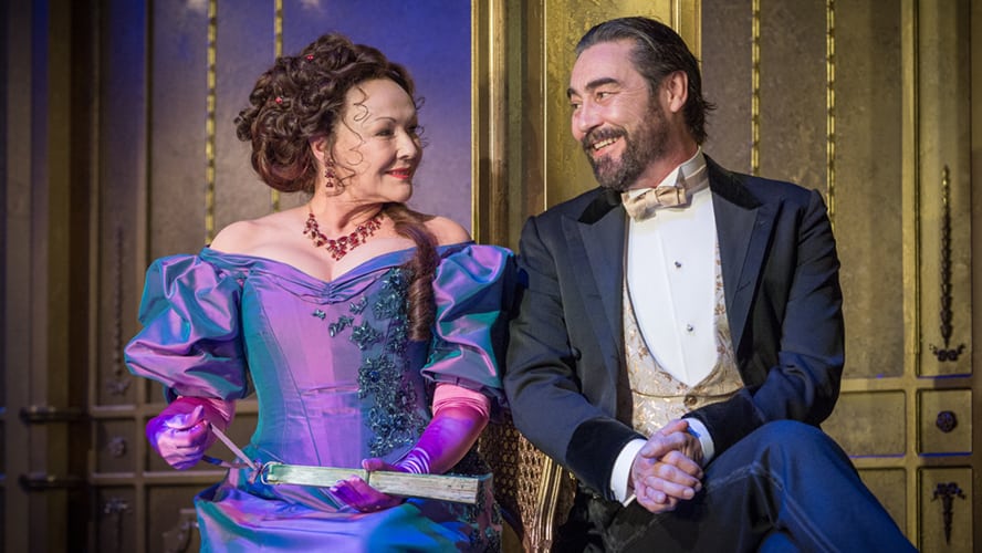 A theatrical scene featuring two characters in period costumes engaged in conversation on stage.