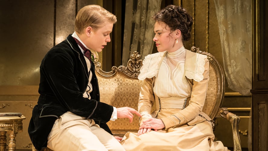A scene from "An Ideal Husband" featuring actors in period costumes on a stage.