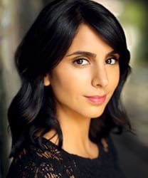Anjli Mohindra smiling, wearing a black top, with long dark hair and a neutral background.