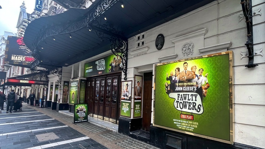 Foyer of Apollo Theatre featuring promotional materials for Fawlty Towers. Elegant decor and lighting visible.