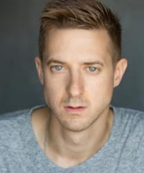 Arthur Darvill smiling, wearing a dark jacket and a patterned shirt, with short hair and a beard.
