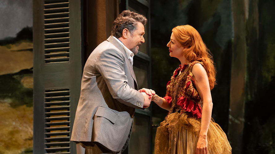 A dramatic scene from Aspects of Love, featuring actors on stage with vibrant lighting.