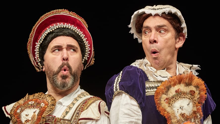 A vibrant stage scene featuring actors in historical costumes performing in front of an audience.
