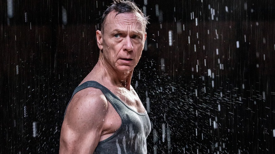 Ben Daniels as Medea, wearing a dramatic costume, stands centre stage with intense expression.