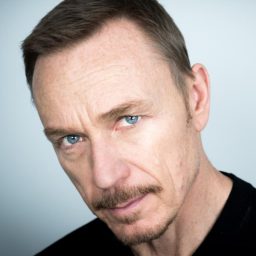 Headshot of a man with short brown hair and a friendly smile, wearing a blue shirt.