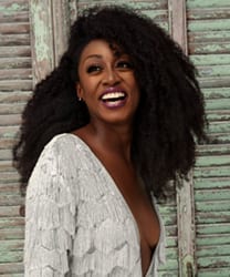 Beverley Knight smiling, with shoulder-length dark hair and wearing a black top against a neutral background.