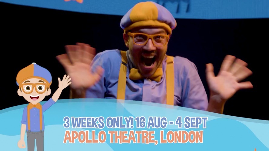 Blippi performing on stage, surrounded by colourful props and enthusiastic children in the audience.