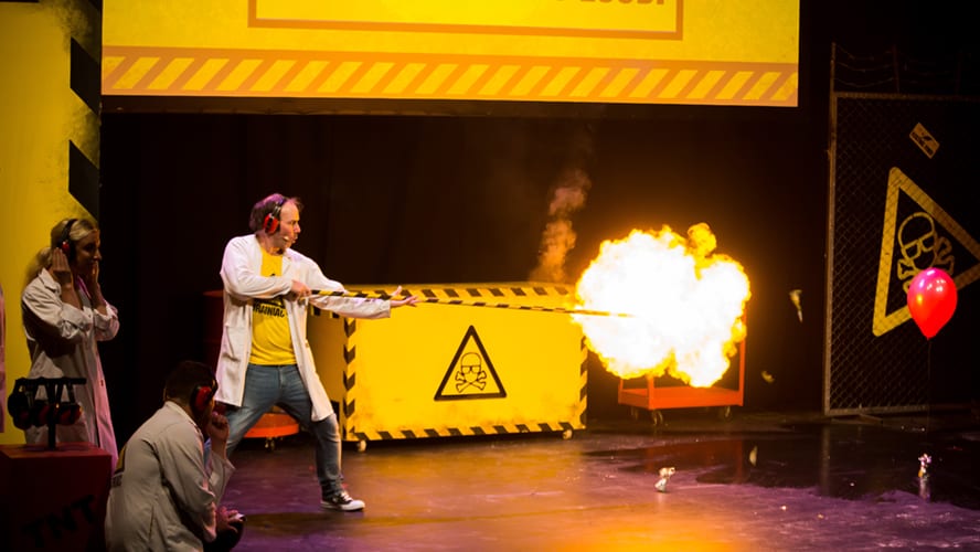 A vibrant stage set with colourful lights and props, featuring performers engaging the audience.