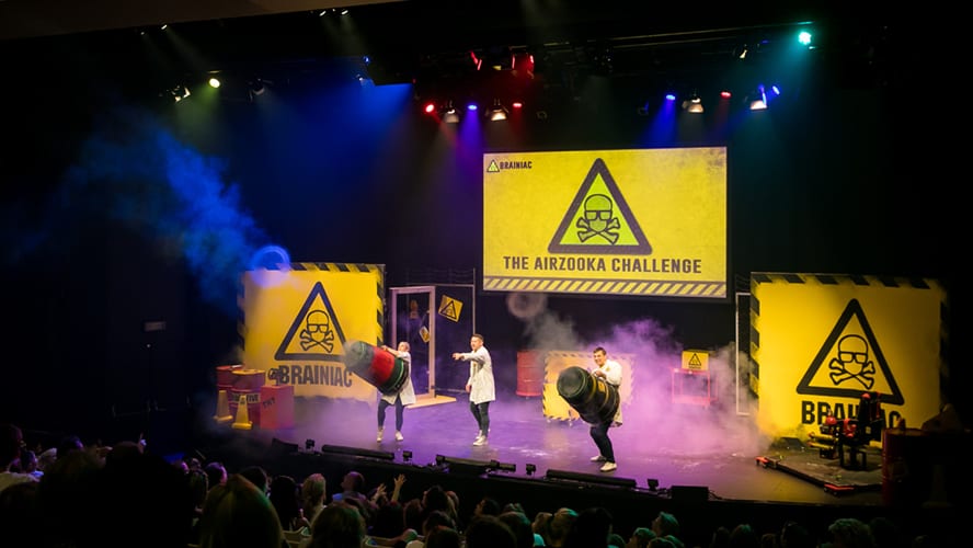 A vibrant stage set with colourful lights and props, featuring performers engaging with the audience.