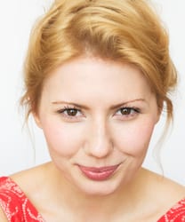 Bronté Barbé smiling, wearing a black blazer and white blouse, with long brown hair.
