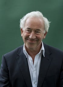 Simon Callow, a distinguished actor, smiling with short dark hair and wearing a black suit.