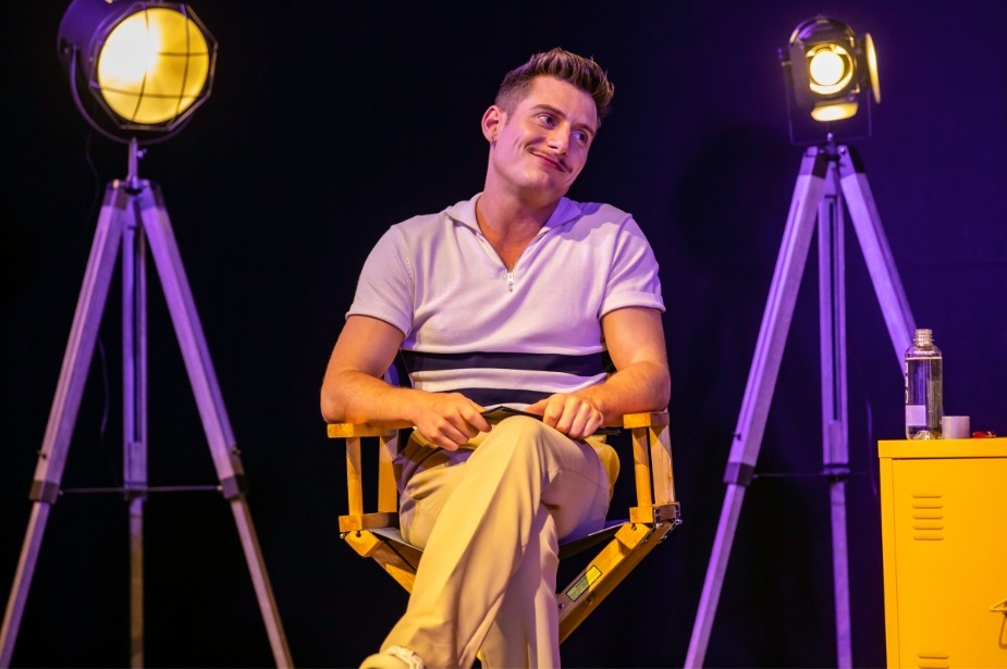Captain Sandy speaking on stage, illuminated by soft lighting, with a microphone in hand.