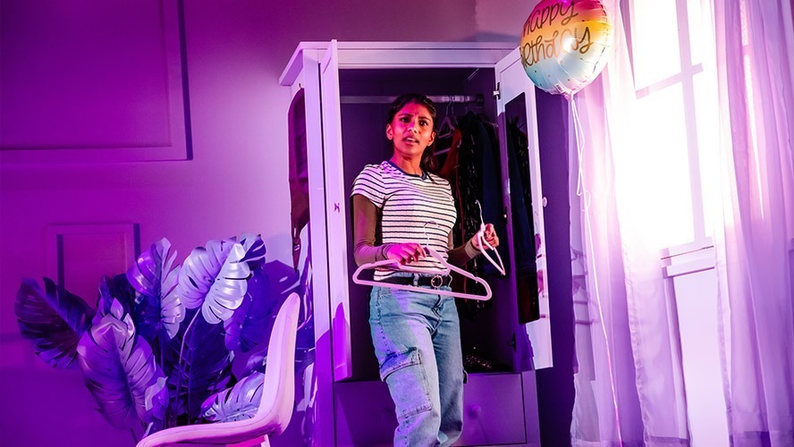 Charithra Chandran smiles, wearing a casual outfit, surrounded by vibrant, colourful set decorations.