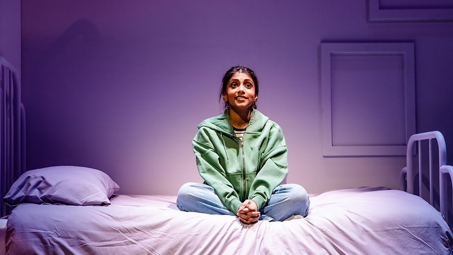 Charithra Chandran smiling, wearing a casual outfit, seated in a bright, modern setting.