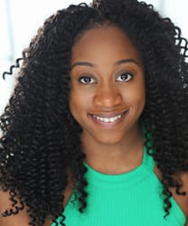 Consuela Rolle smiling, wearing a blue blouse, with long dark hair and a neutral background.