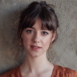 Daisy Edgar-Jones smiling, with long brown hair and a neutral background.
