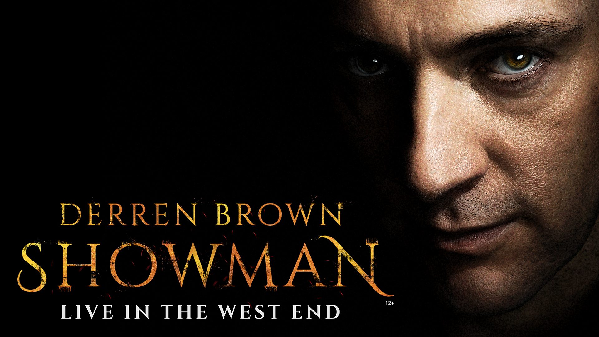 Derren Brown performing on stage, illuminated by dramatic lighting, with an audience visible in the background.