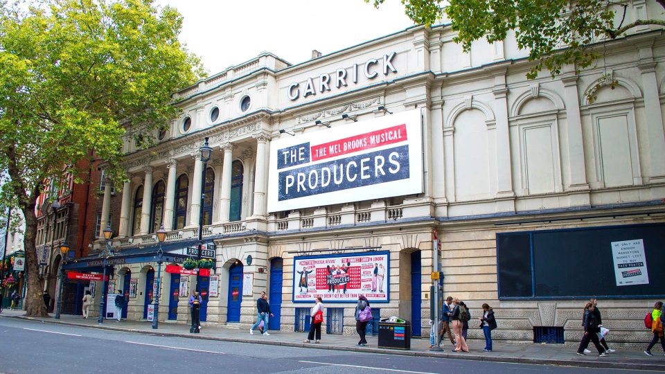 Garrick Theatre's façade features a large promotional banner for "The Producers" against a grey sky.