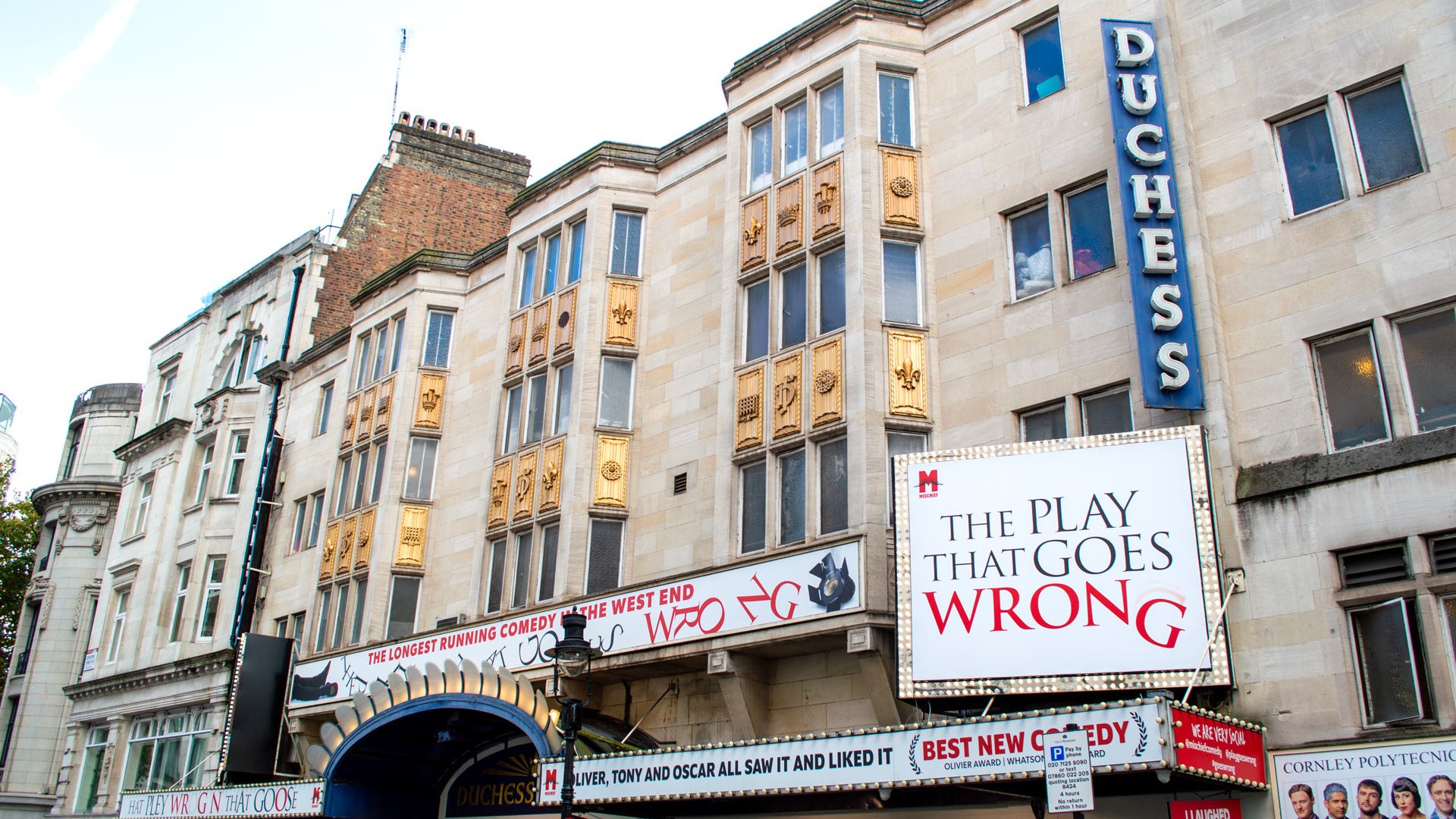 Duchess Theatre exterior featuring cream stone, decorative gold accents, and a prominent show banner.