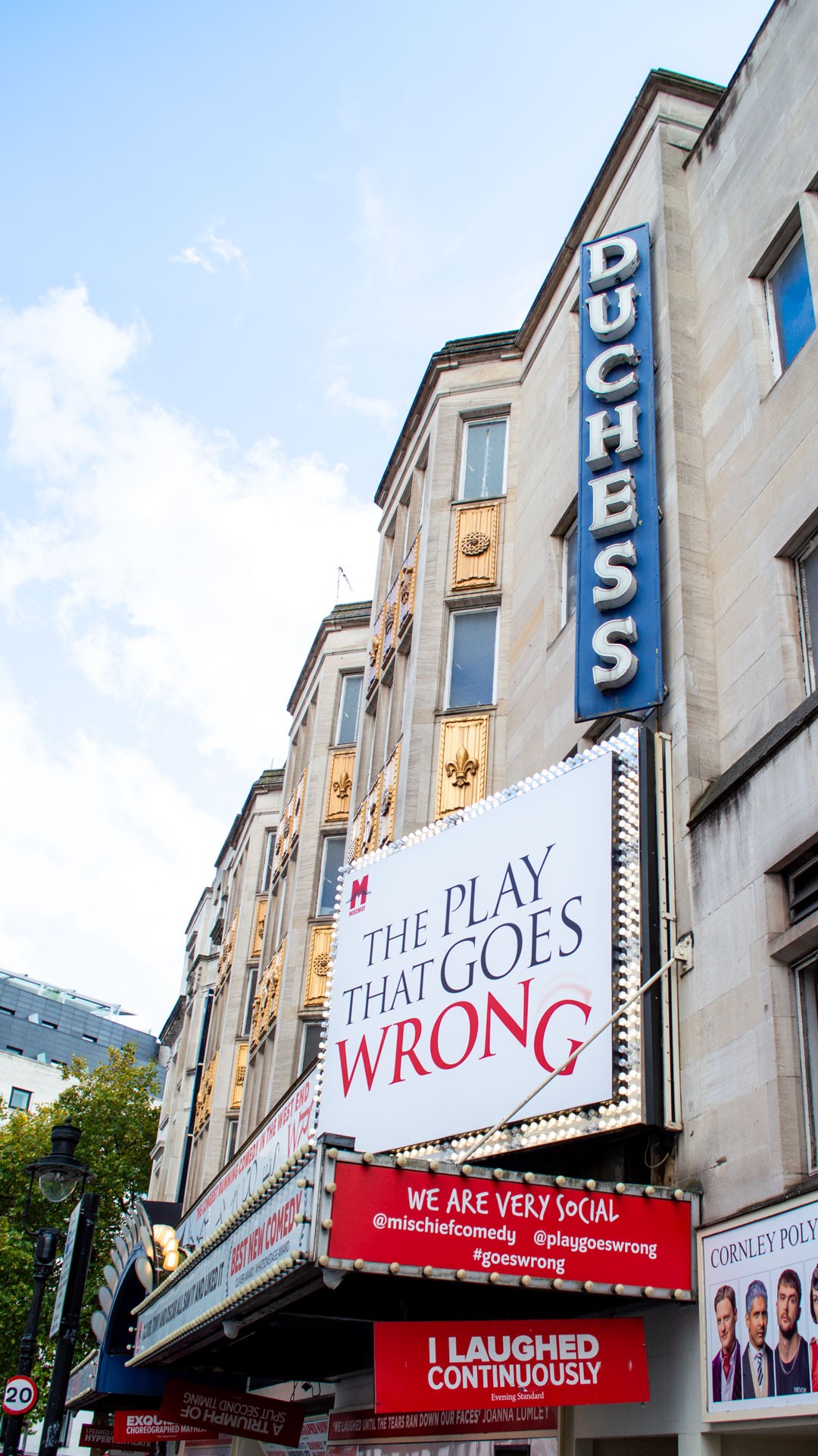Duchess Theatre exterior featuring a bright marquee for "The Play That Goes Wrong" against a blue sky.