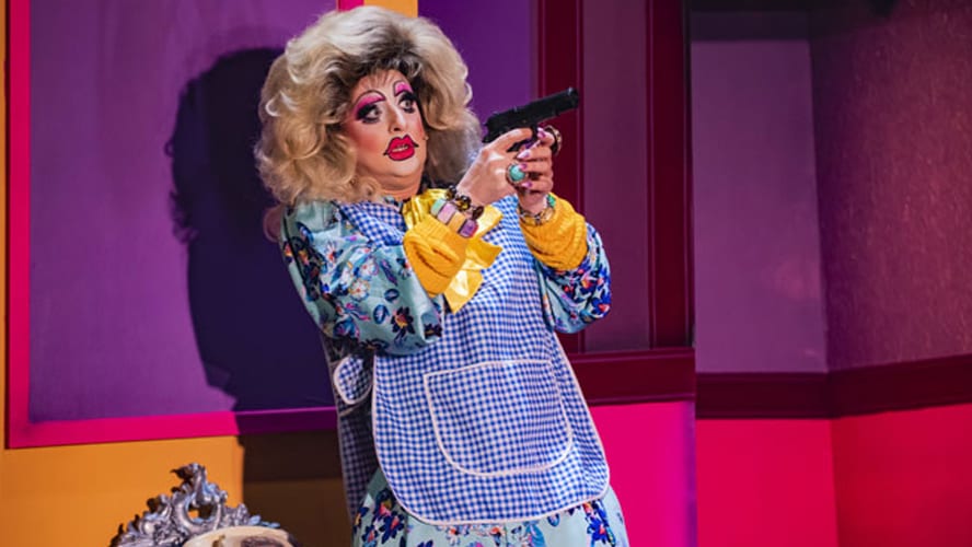 A performer executing a dramatic death drop on stage, wearing a vibrant costume and dramatic makeup.