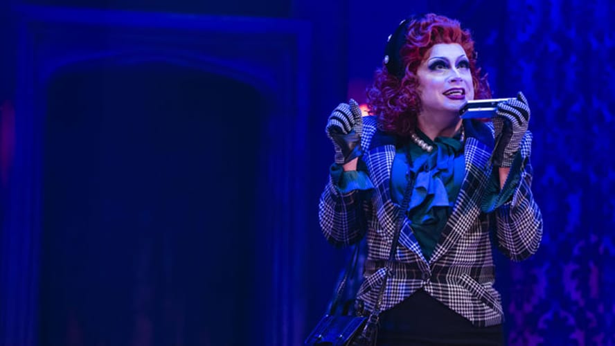 A performer executing a dramatic death drop on stage, wearing a vibrant costume and dramatic makeup.