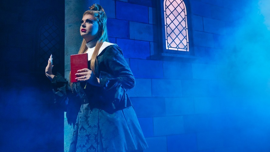 A theatrical scene featuring actors in vibrant costumes performing on a stage with dramatic lighting.