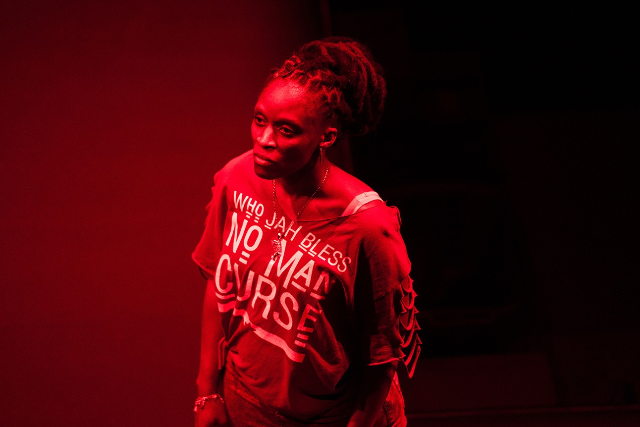 A dramatic stage scene featuring actors in intense expressions, with dim lighting and a minimalist set.
