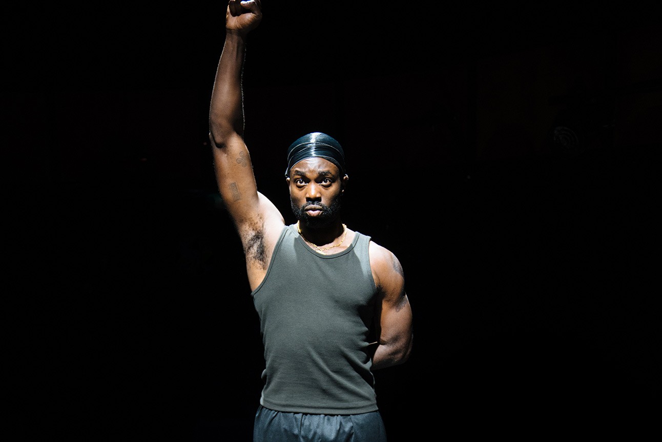 A dramatic stage scene featuring a male actor in a spotlight, expressing intense emotion.