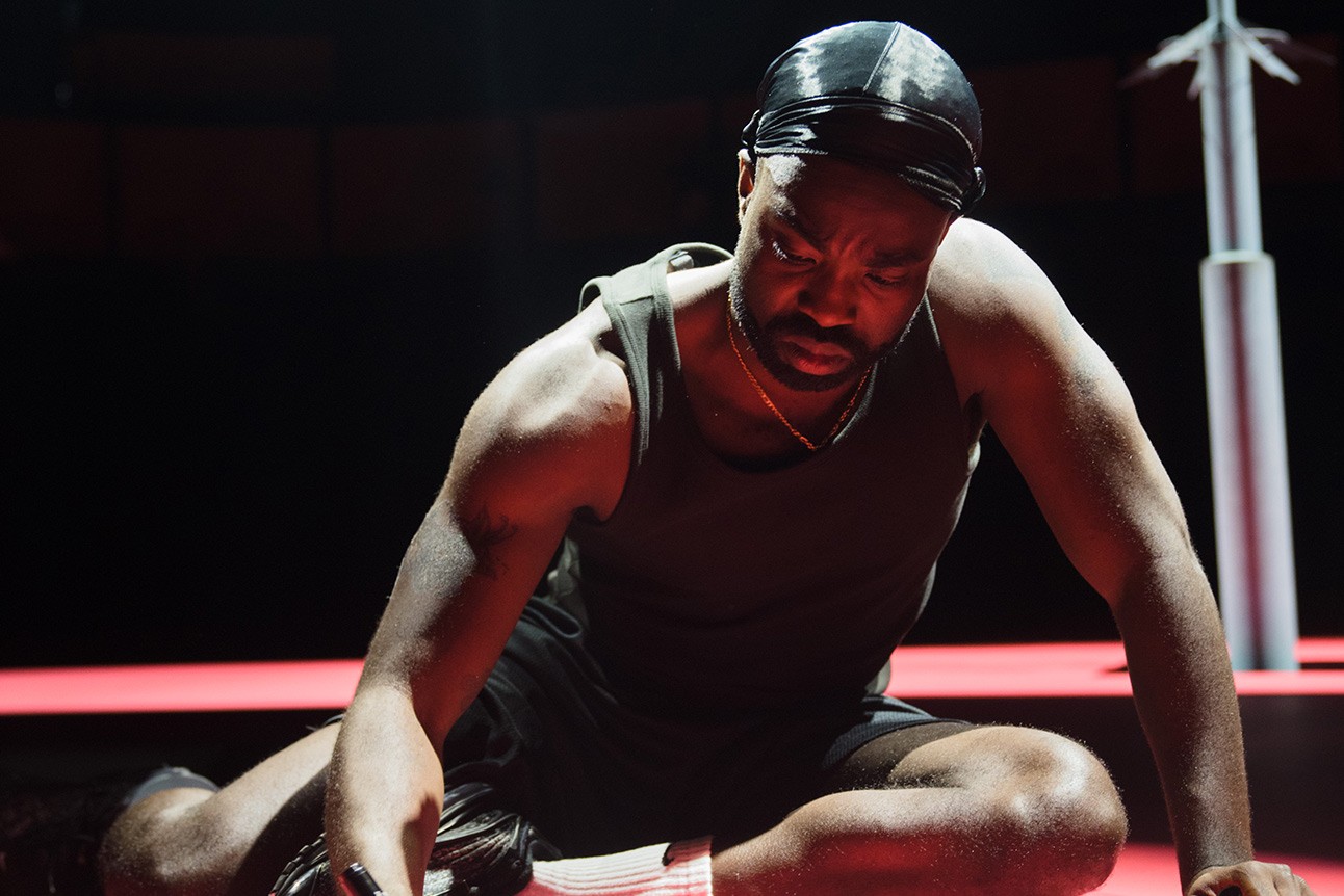 A theatrical scene featuring a male actor in a dramatic pose on stage, with dim lighting.