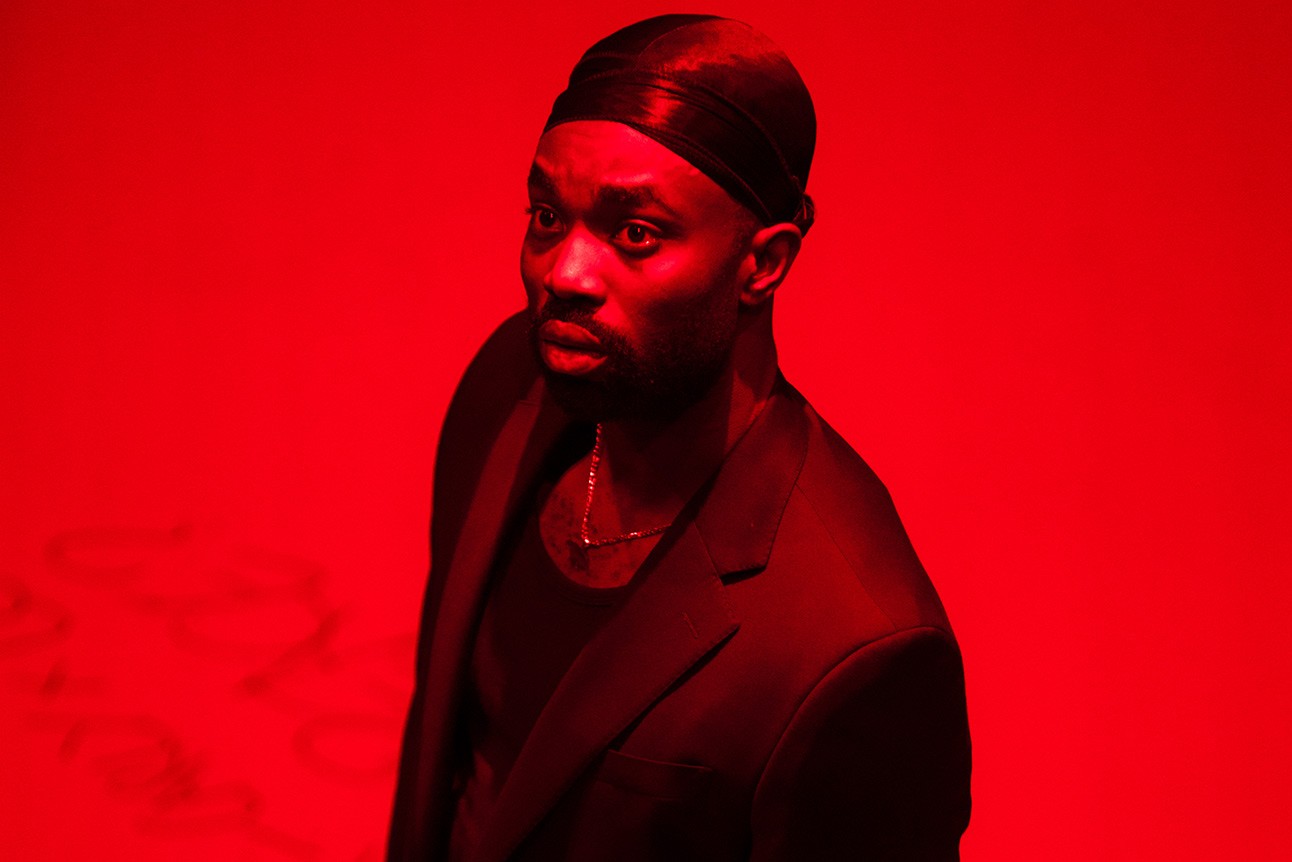 A dramatic stage scene featuring a male actor in a suit, expressing intense emotion.