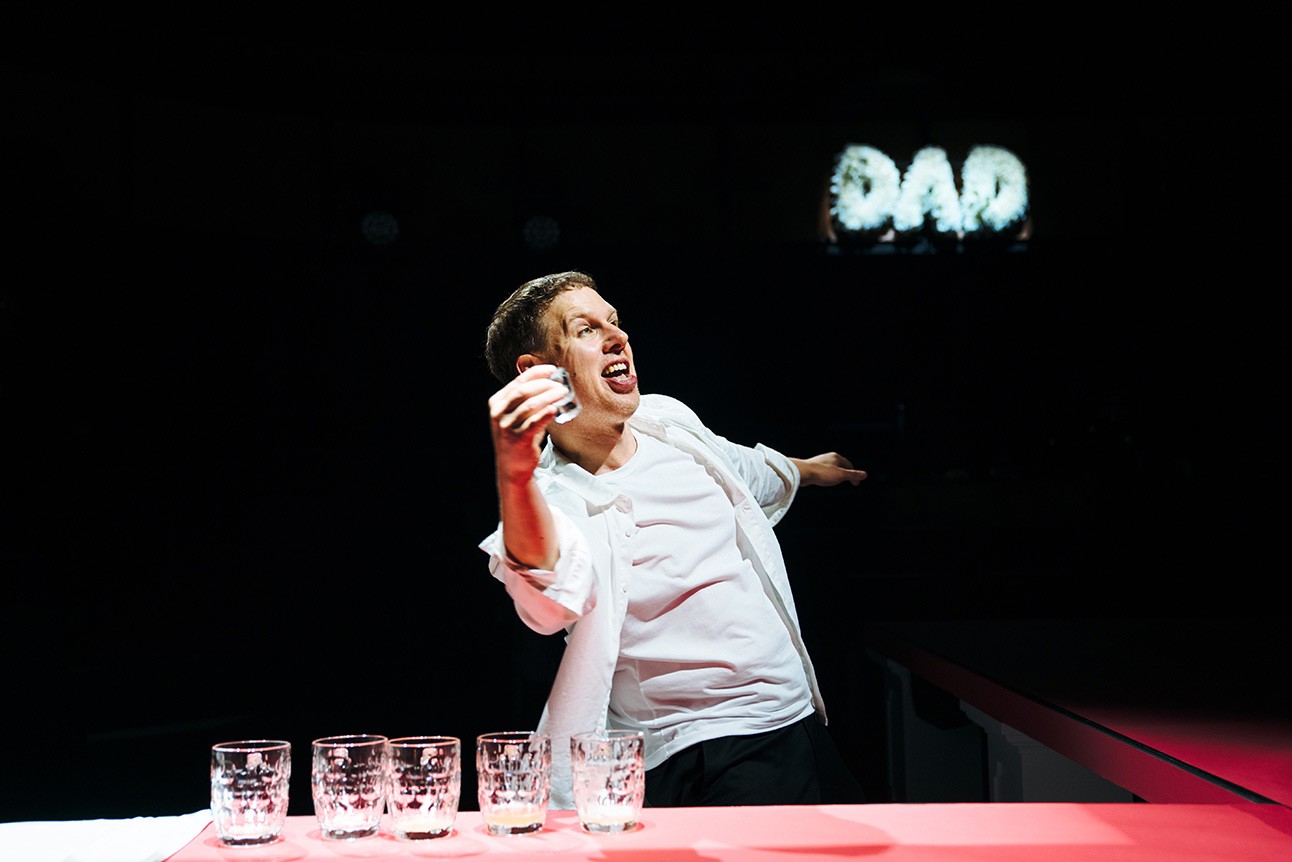 A theatrical scene featuring actors in dramatic costumes, set against a minimalist stage backdrop.