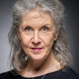 Debra Lawrance smiling, wearing a black dress, with long hair styled elegantly.