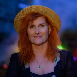 Eddi Reader smiling, with a blurred background, showcasing her short hair and casual attire.