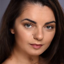 Elena Pitsiaeli smiling, wearing a blue blouse, with long dark hair and a neutral background.