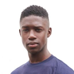 Headshot of Emeka Sesay, featuring a professional smile and a dark suit against a neutral background.